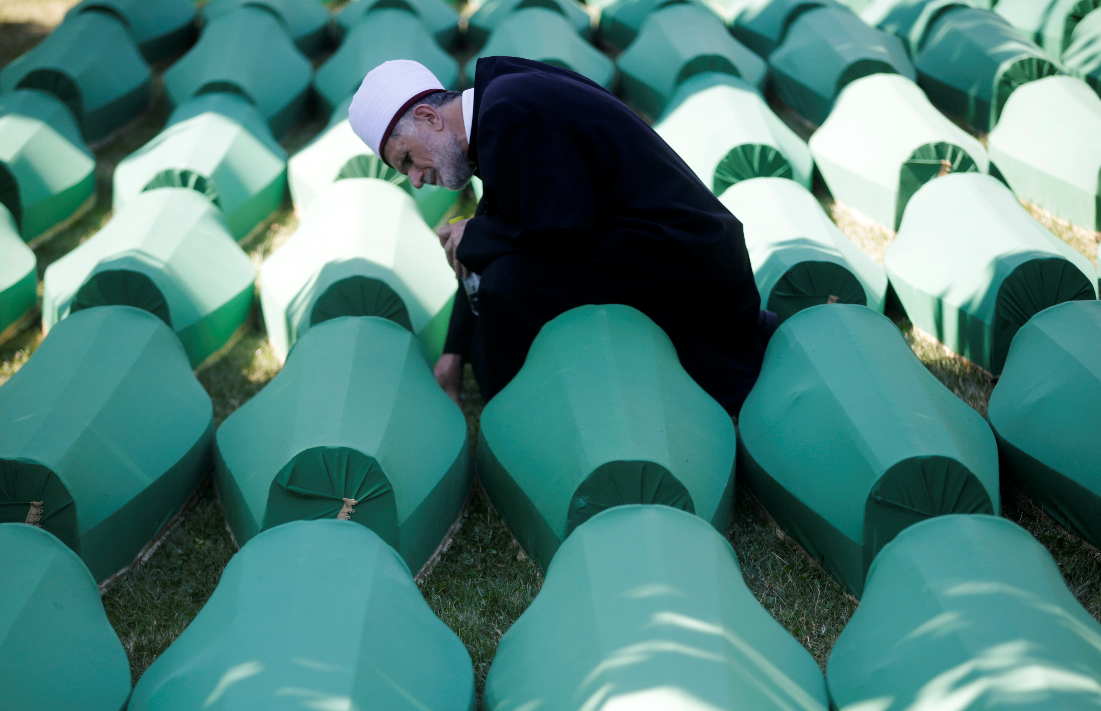 Muslim effendi sits near coffins of his relatives, who are newly identified victims of the 1995 Srebrenica massacre, which are lined up for a joint burial in Potocari near Srebrenica