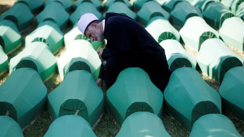 Muslim effendi sits near coffins of his relatives, who are newly identified victims of the 1995 Srebrenica massacre, which are lined up for a joint burial in Potocari near Srebrenica