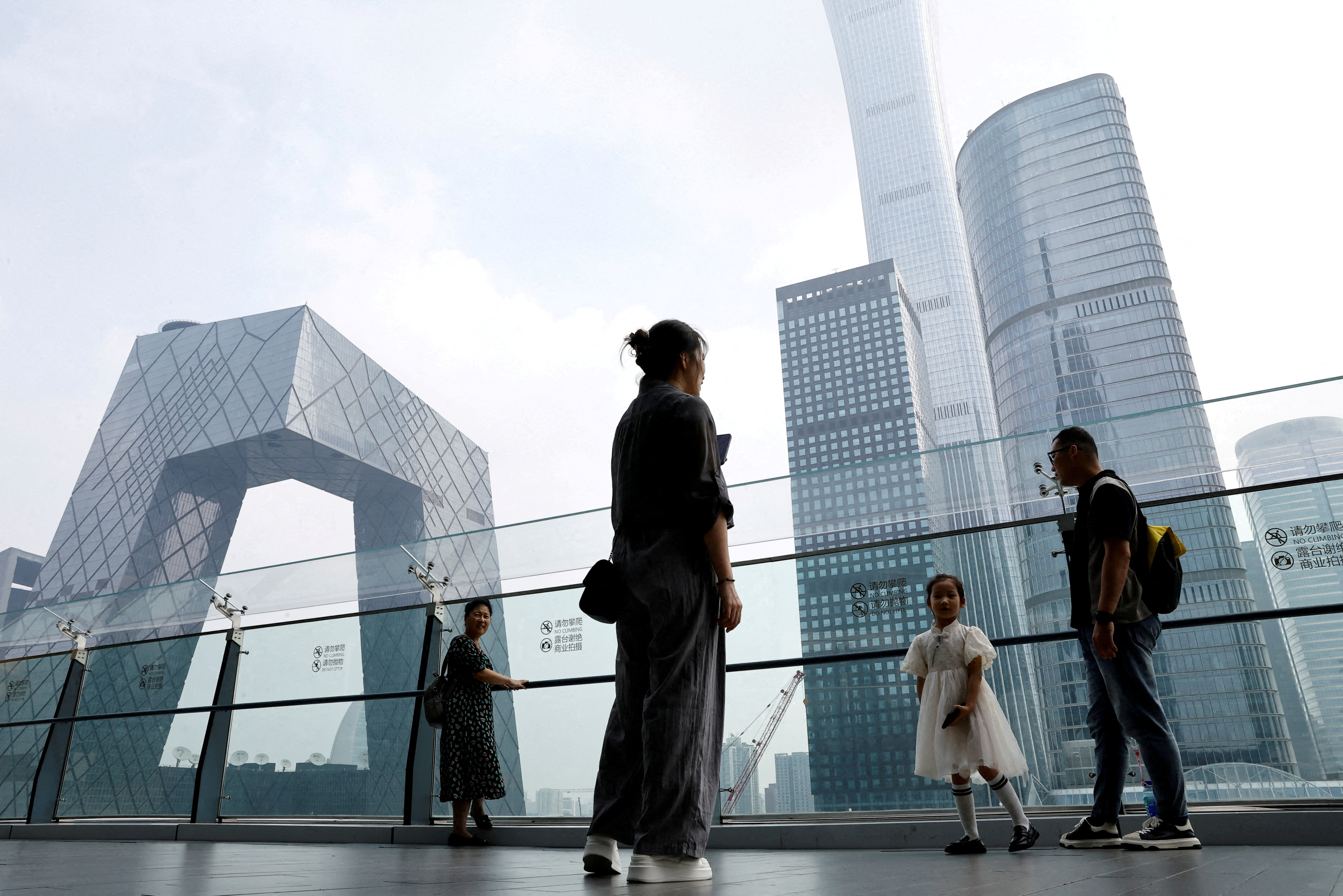 FILE PHOTO: People stand at a shopping mall near the CCTV headquarters and China Zun skyscraper, in Beijing's central business district (CBD)