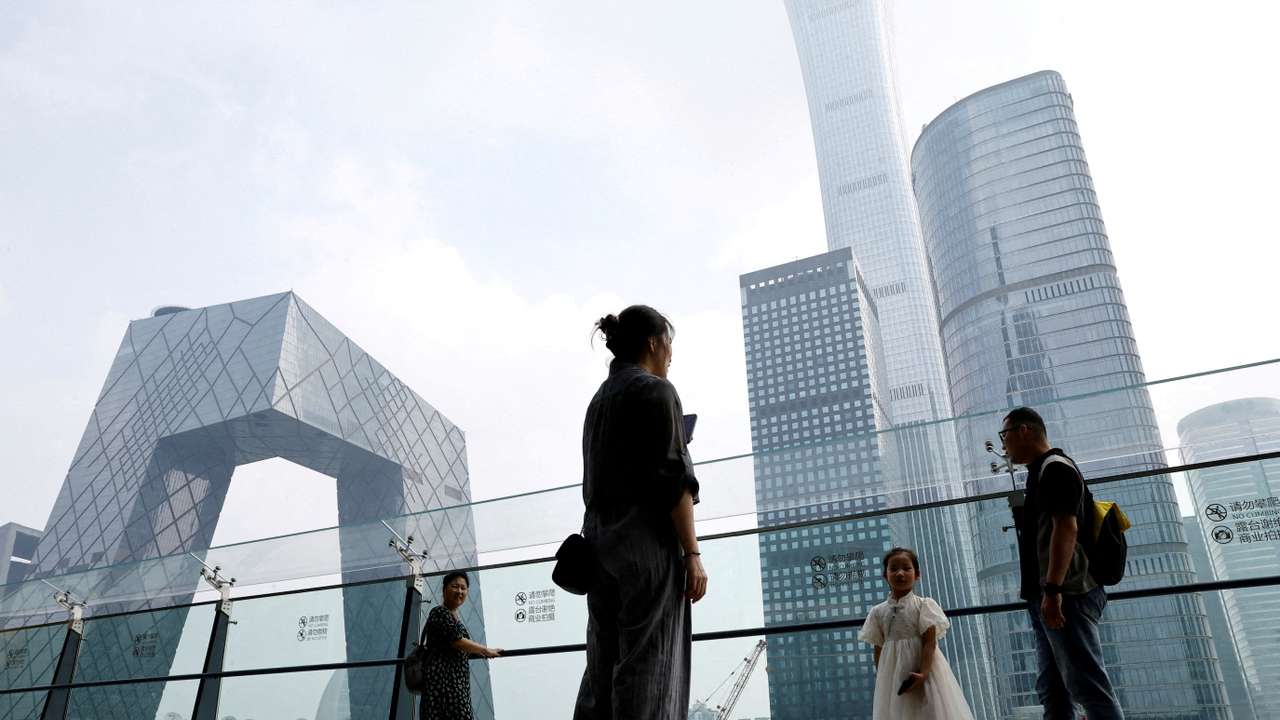 FILE PHOTO: People stand at a shopping mall near the CCTV headquarters and China Zun skyscraper, in Beijing's central business district (CBD)