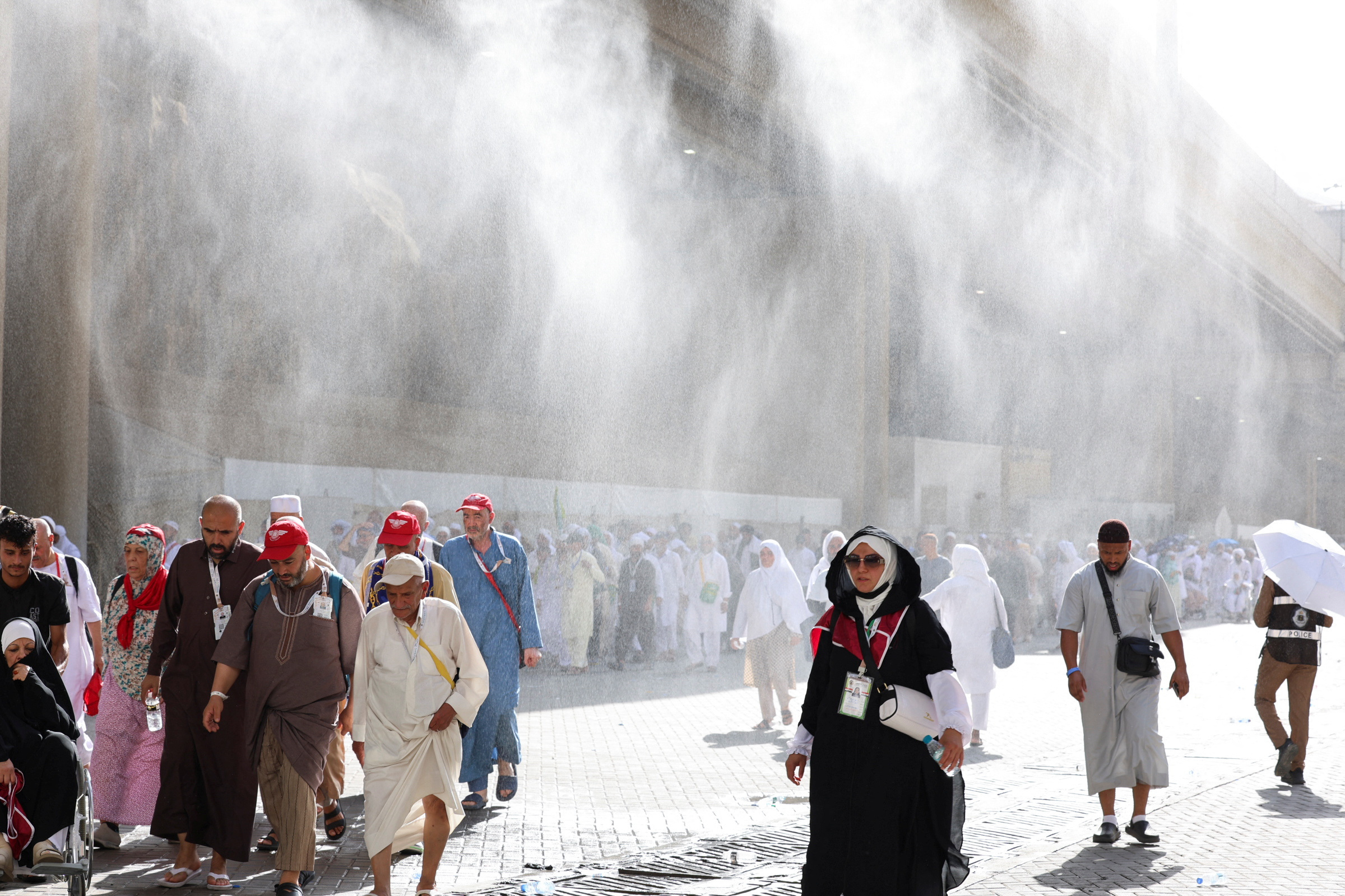 Muslim pilgrims walk as water sprinklers spray water during the annual hajj pilgrimage in Mina