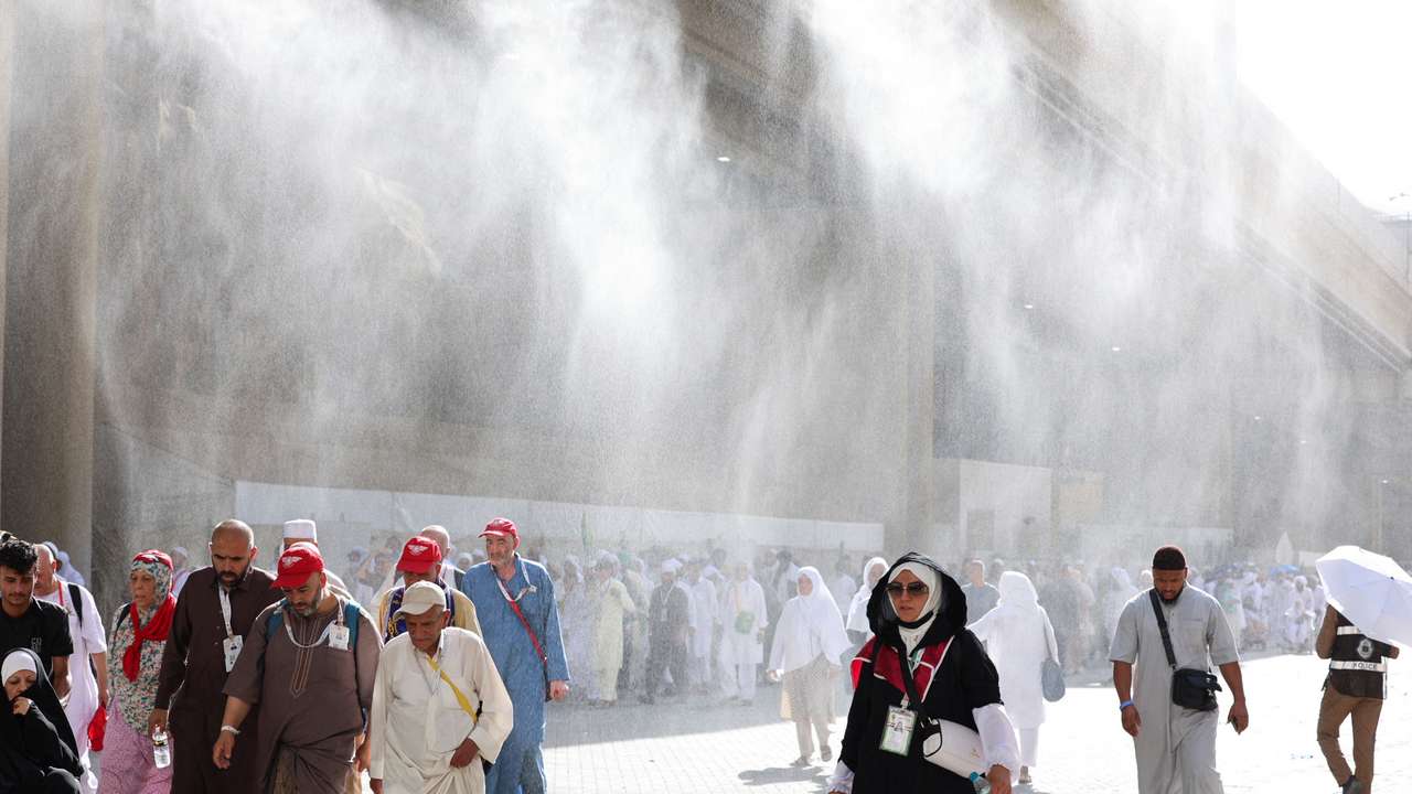 Muslim pilgrims walk as water sprinklers spray water during the annual hajj pilgrimage in Mina
