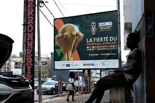A man stares at an official AFCON poster. Abidjan, 2024.