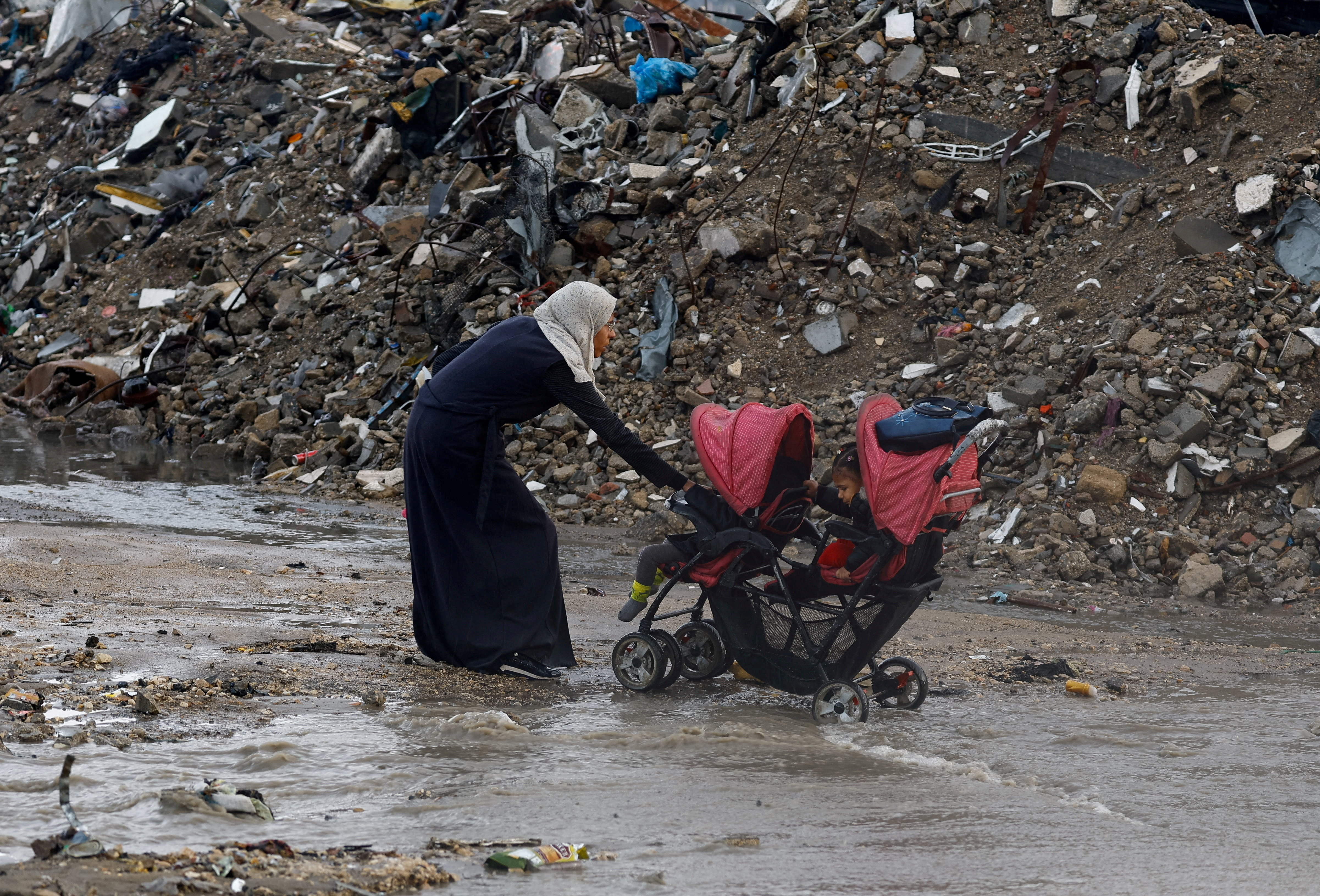 A Palestinian woman pulls a stroller with children, during a rainy day in Gaza City