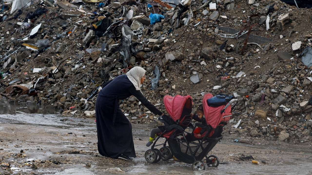 A Palestinian woman pulls a stroller with children, during a rainy day in Gaza City