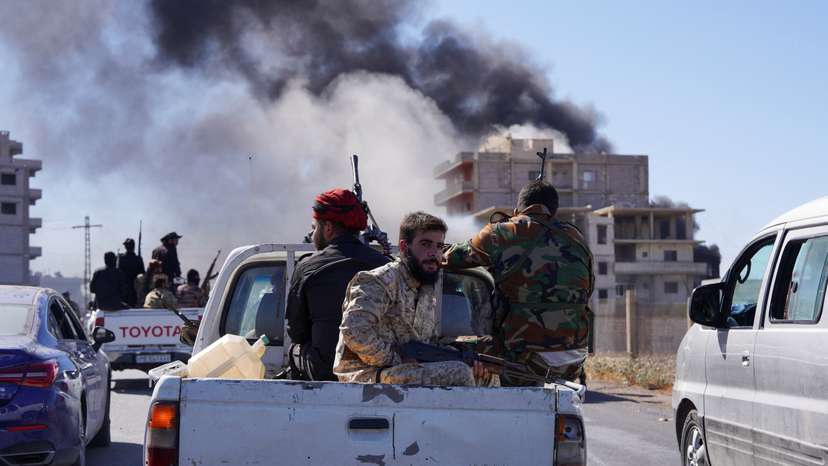 Smoke rises while Syrian security forces sit in the back of a truck, in Sweida