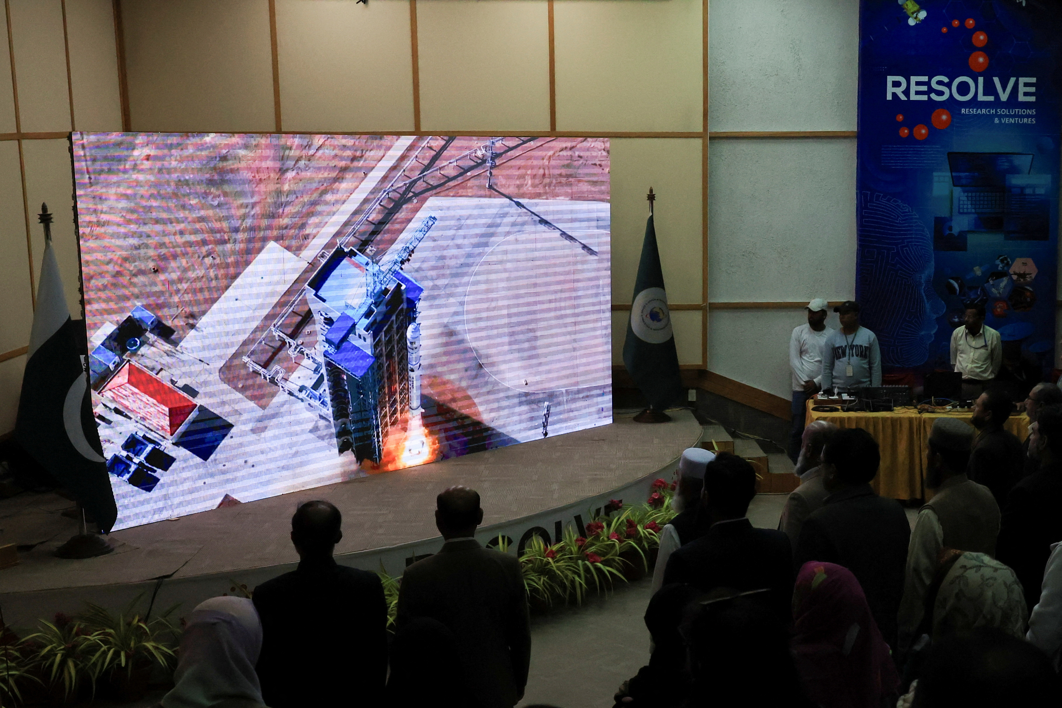 People watch a screen displaying the launch of Pakistan's Electro-Optical (EO-1) satellite, at the SUPARCO Complex, in Karachi