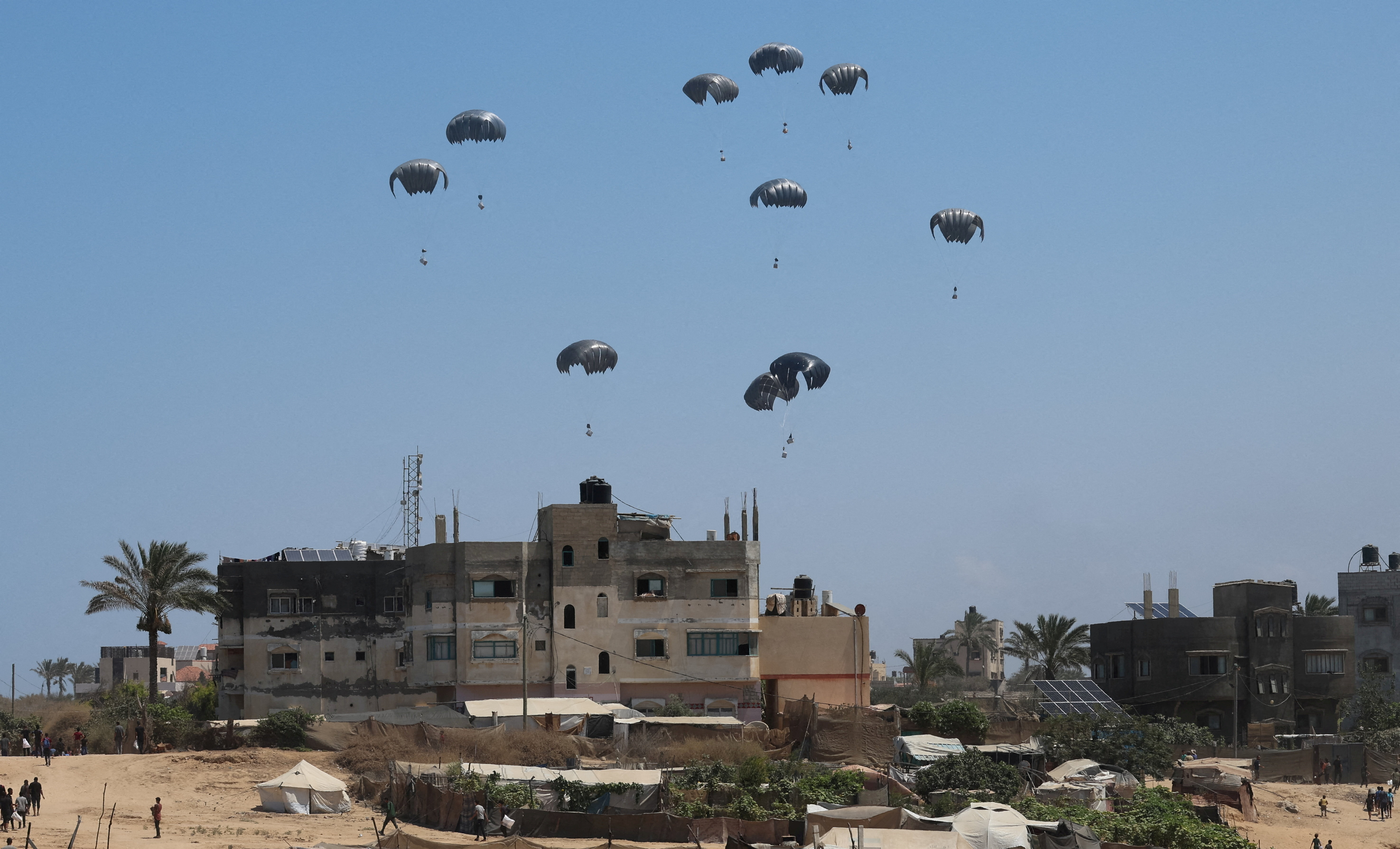 Aid packages dropped from an airplane descend over Gaza, in Zawayda