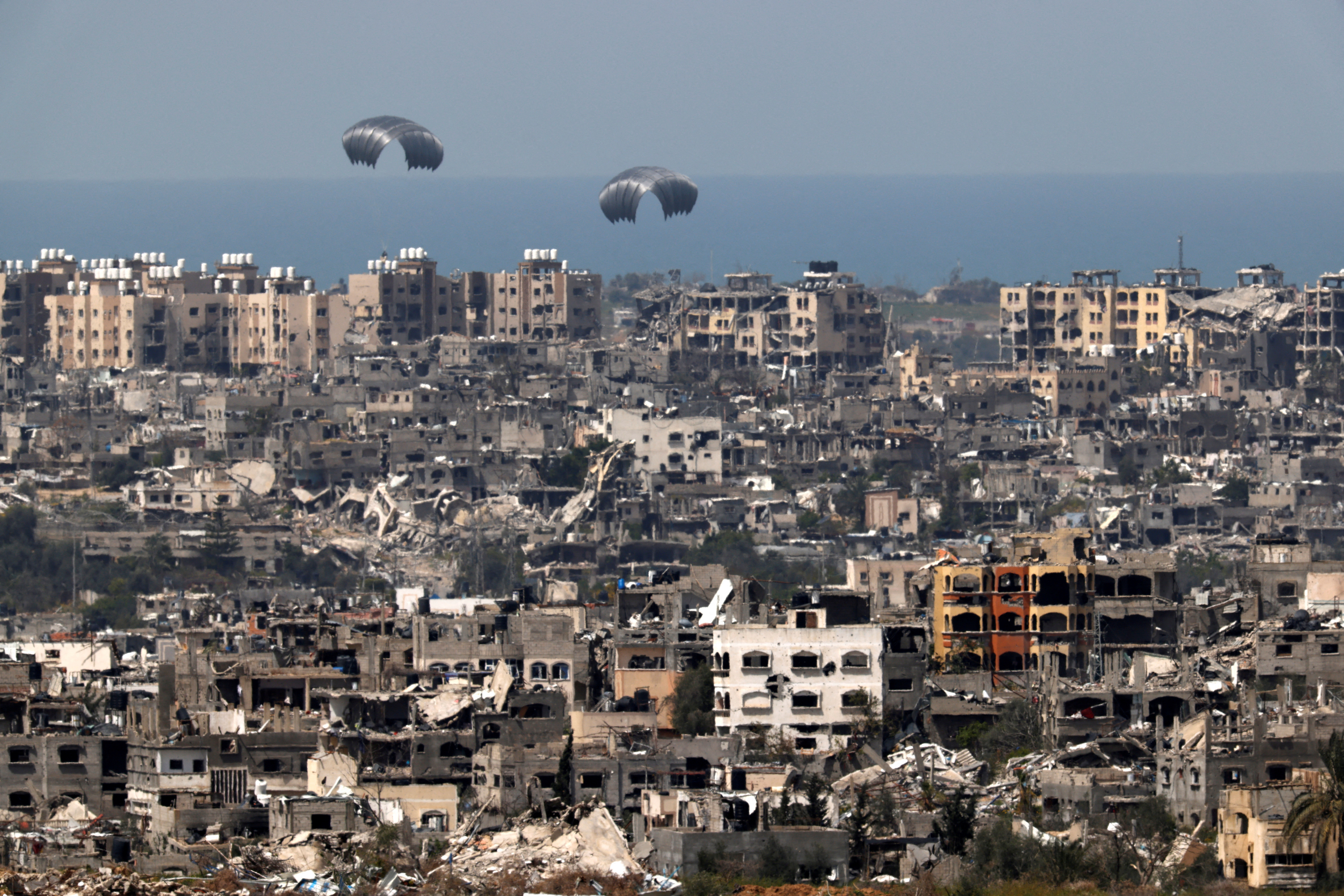 Humanitarian aid falls through the sky towards the Gaza Strip, as seen from Israel's border with Gaza
