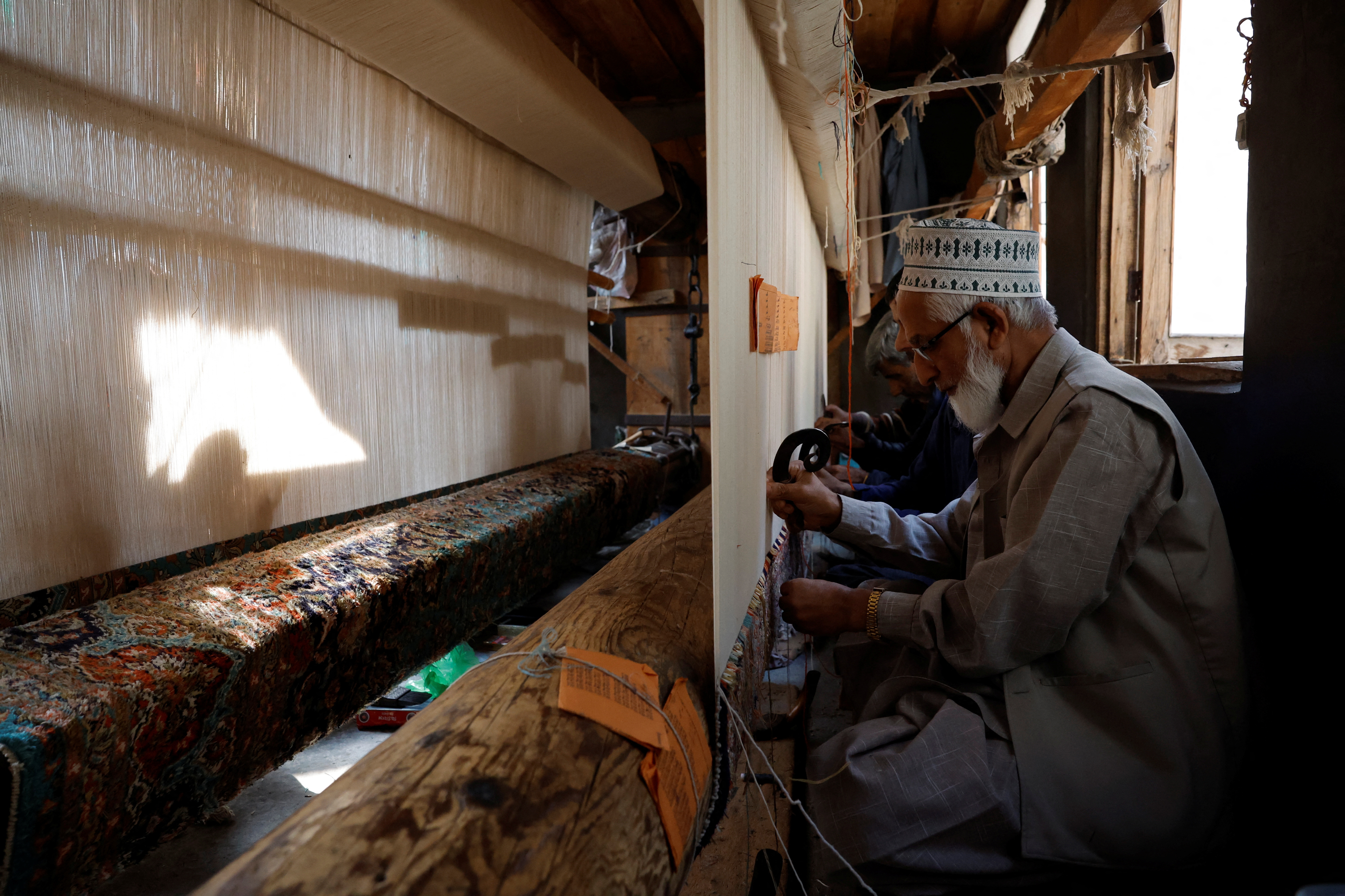 Ghulam Qadir, 75, an artisan, weaves a Kashmiri hand-knotted carpet along with other artisans inside a workshop in Srinagar