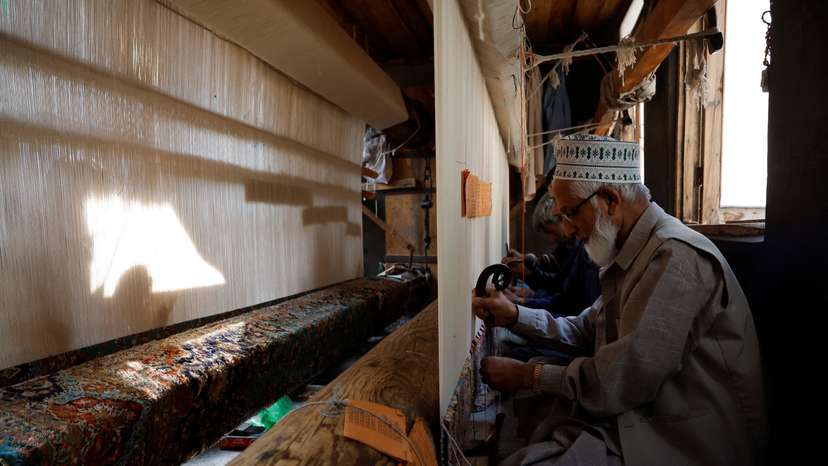 Ghulam Qadir, 75, an artisan, weaves a Kashmiri hand-knotted carpet along with other artisans inside a workshop in Srinagar