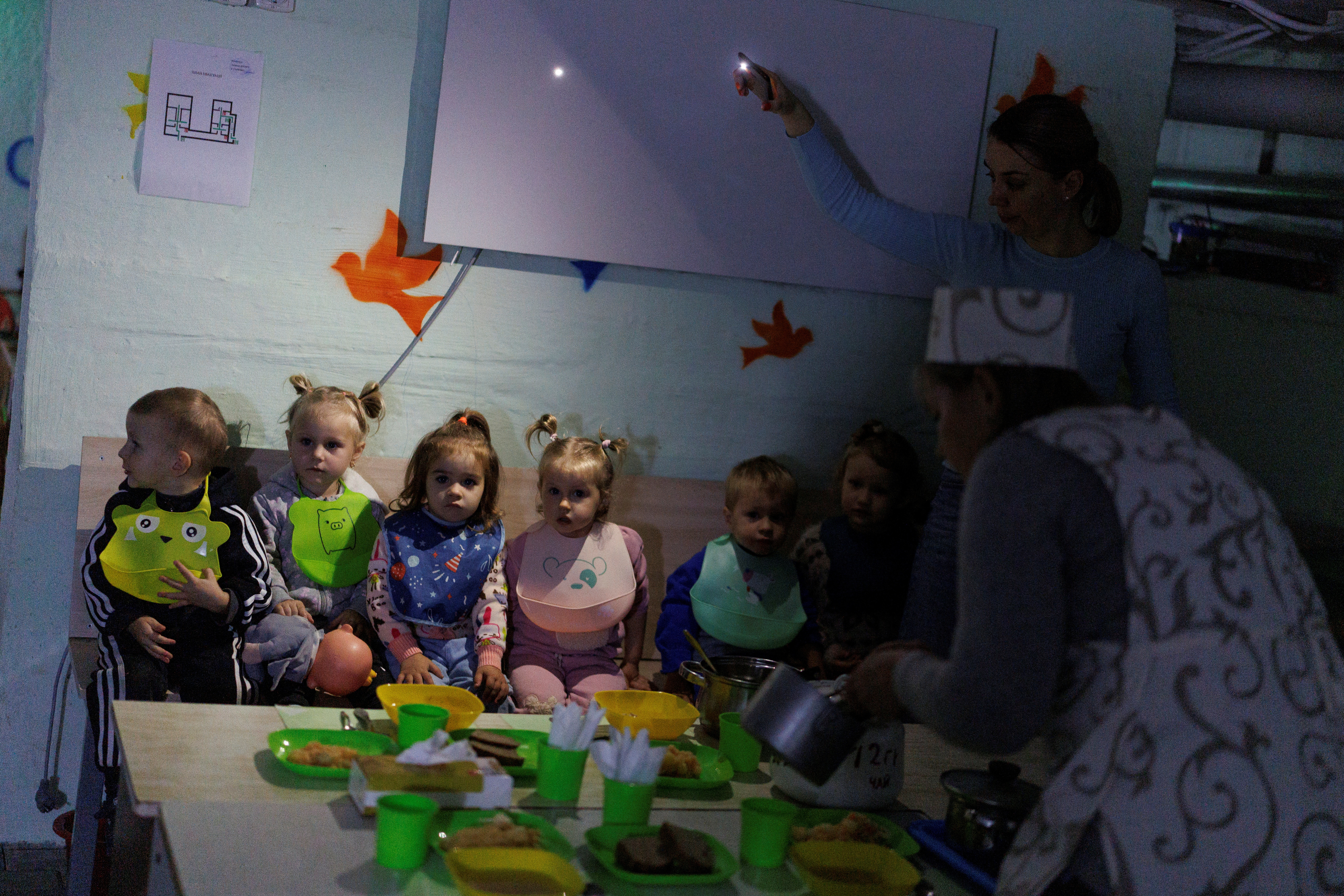 A kindergarten employee serves food on a table to feed children inside a bomb shelter during ongoing air alert and power outage in Chernihiv