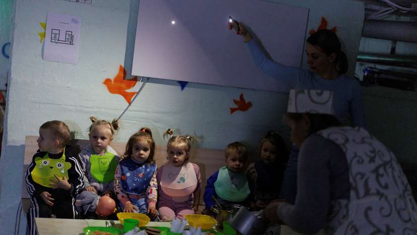 A kindergarten employee serves food on a table to feed children inside a bomb shelter during ongoing air alert and power outage in Chernihiv