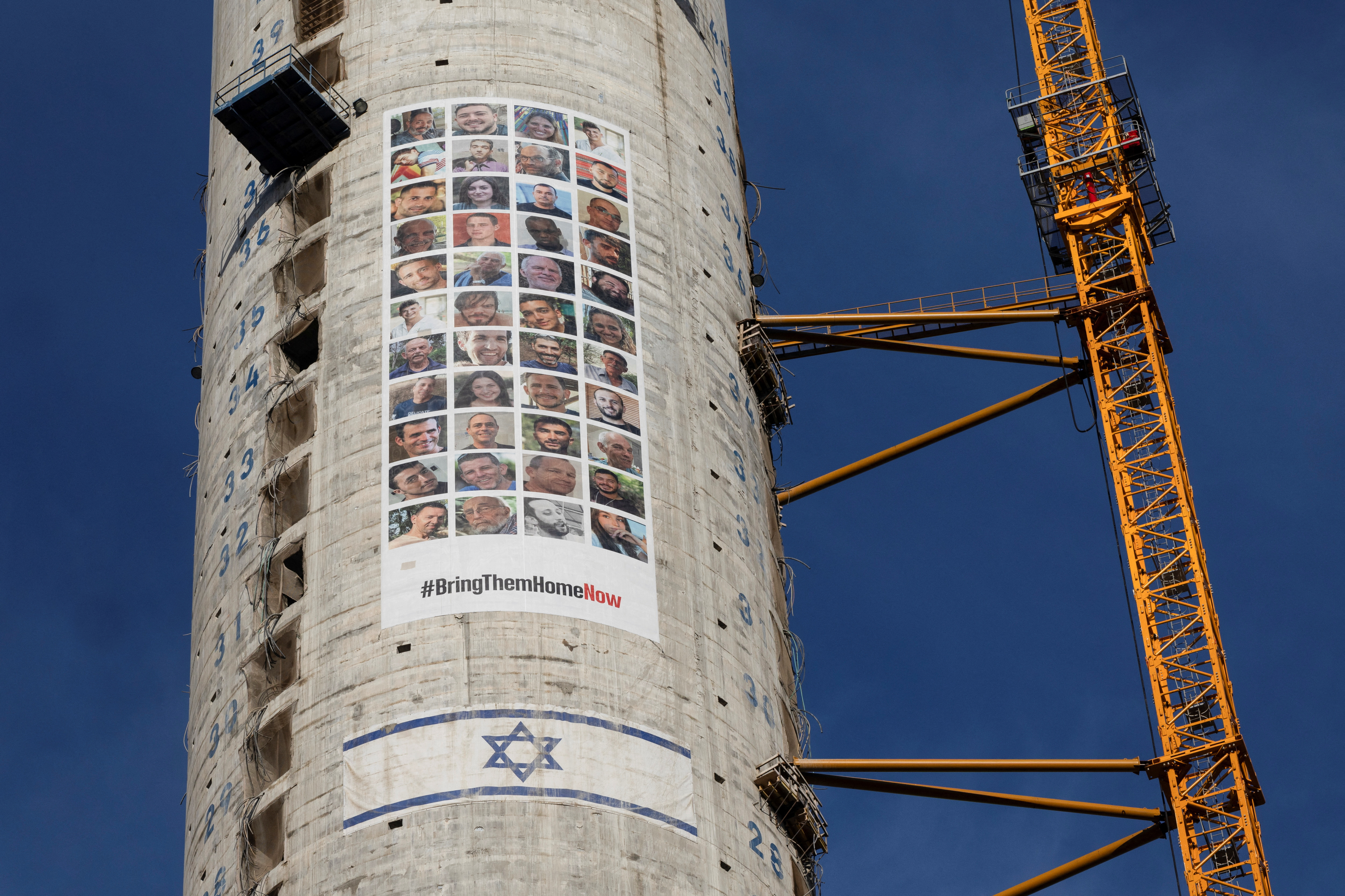 Pictures of hostages kidnapped during the deadly October 7 attack by the Palestinian Islamist group Hamas from Gaza, are seen next to an Israeli flag on a building under construction, in Tel Aviv