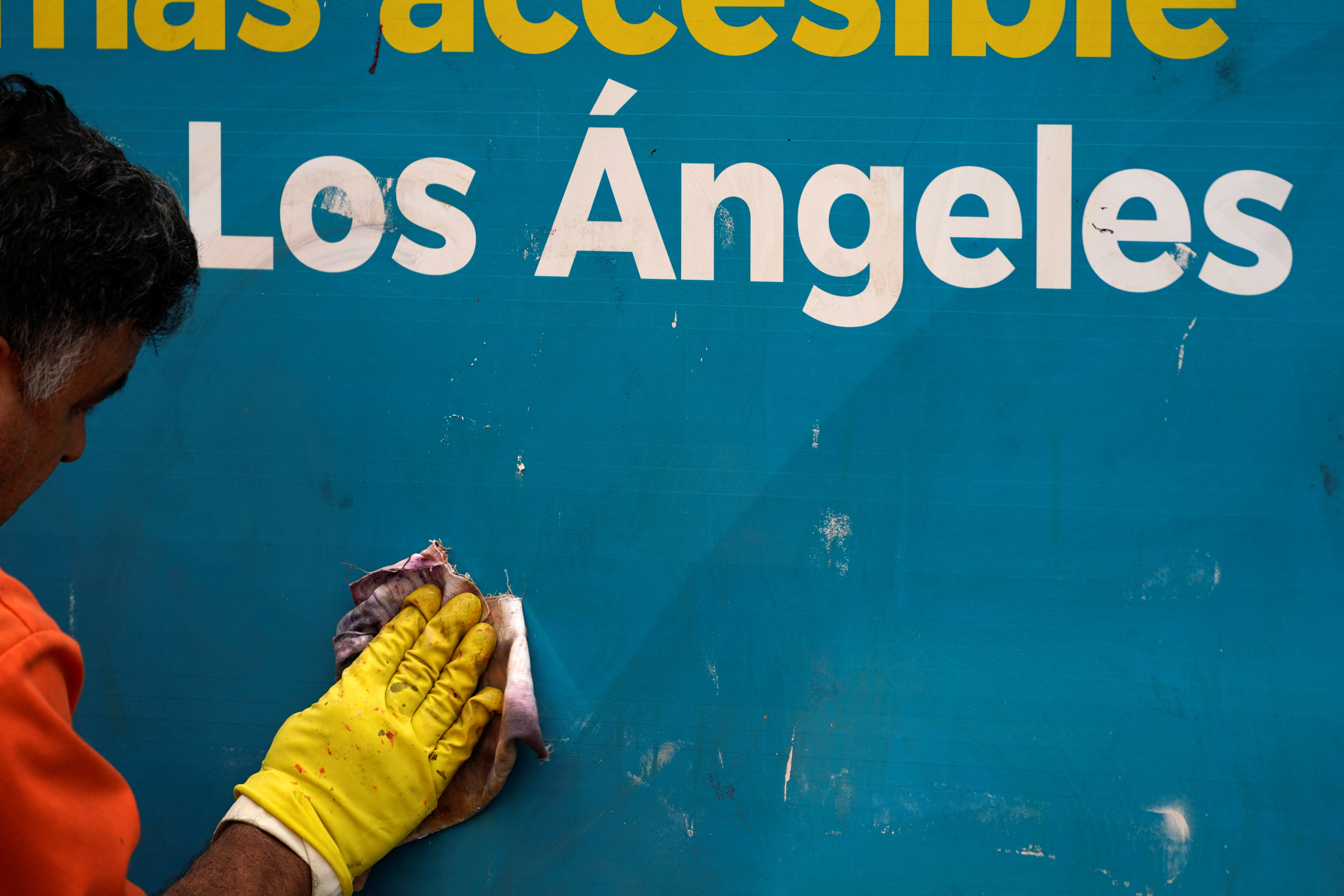 A worker removes graffiti from a sign, as protests against immigration sweeps continue, in Los Angeles,