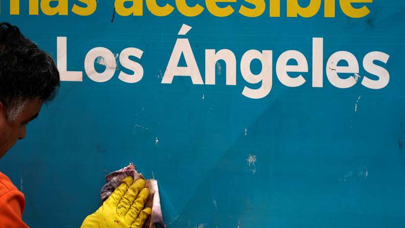 A worker removes graffiti from a sign, as protests against immigration sweeps continue, in Los Angeles,