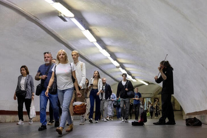 FILE PHOTO: A man plays the violin as people walk in a subway station during morning rush hour in central Kyiv